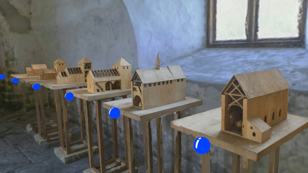 Five wooden models of the church over the years on tables with blue "info" spheres in front of each one