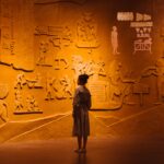 Woman standing near old stone wall with carved images