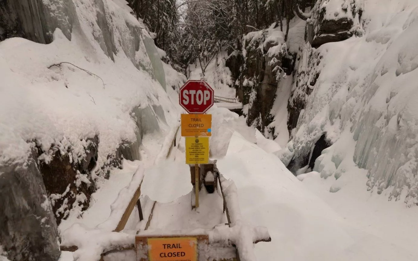 Image of a snow and ice covered bridge with a STOP sign and "Trail Closed" sign
