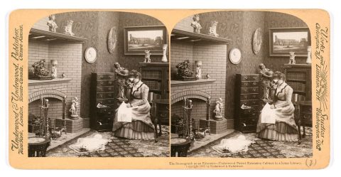 A woman sits at a table using a stereoscope